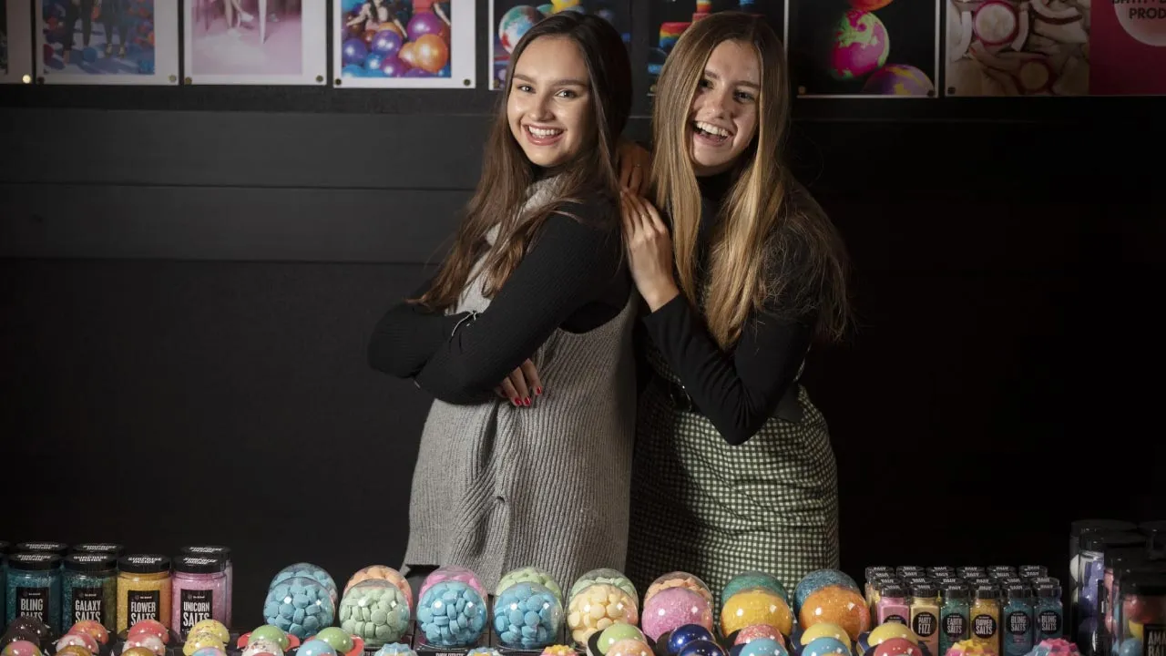 Caroline and Isabel Bercaw, founders of Da Bomb Bath Fizzers side by side with their products displayed in front of them.