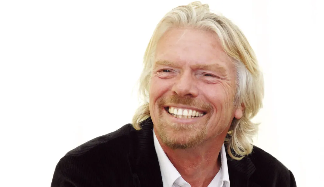 Richard Branson happily smiling wearing a suit in white background.
