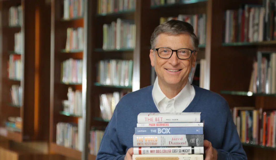 Bill Gates holding his collection of favorite books while smiling at the camera.