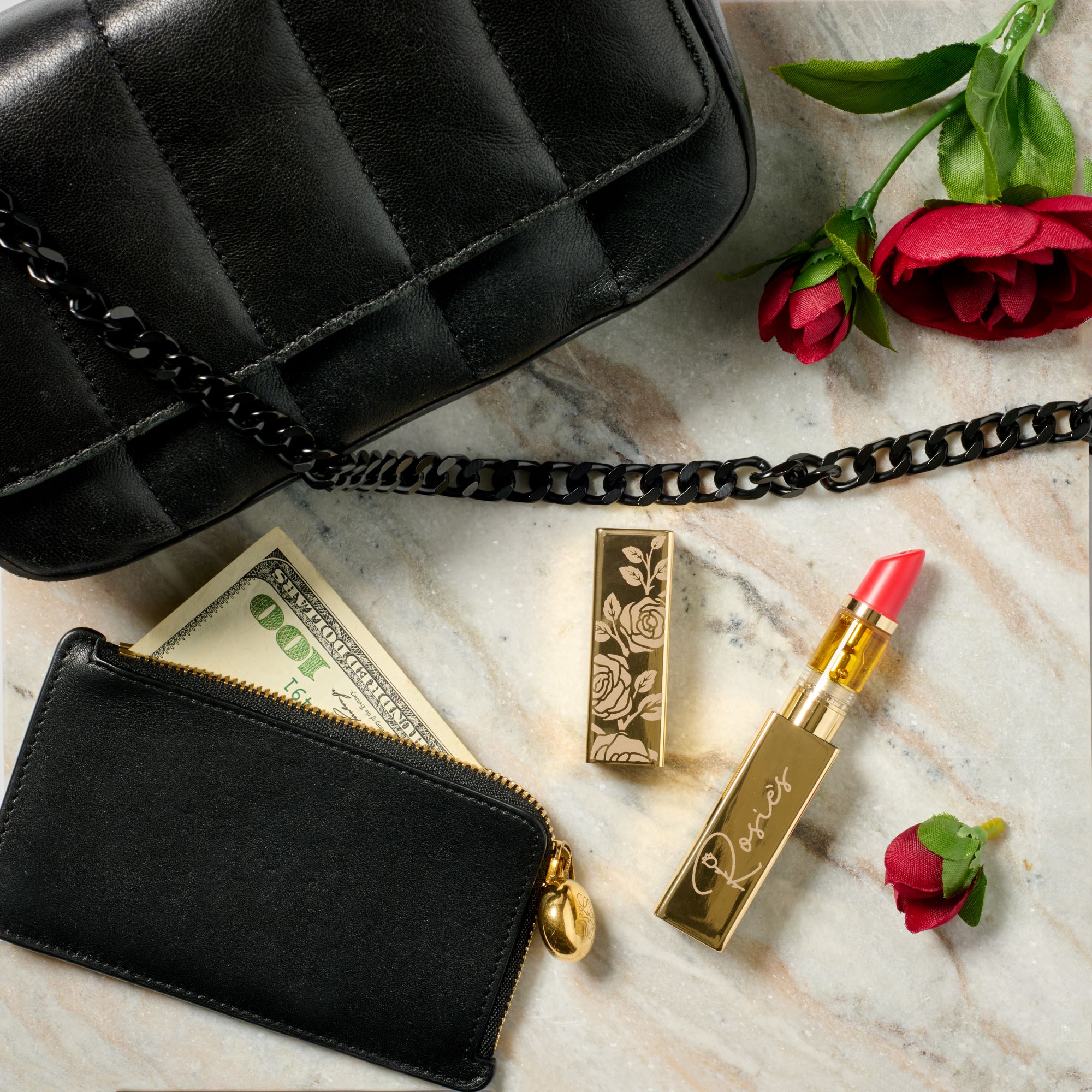 White leather purse with gold bee emblem and chain next to gold lipstick with pink tip and pink flowers on marble surface.