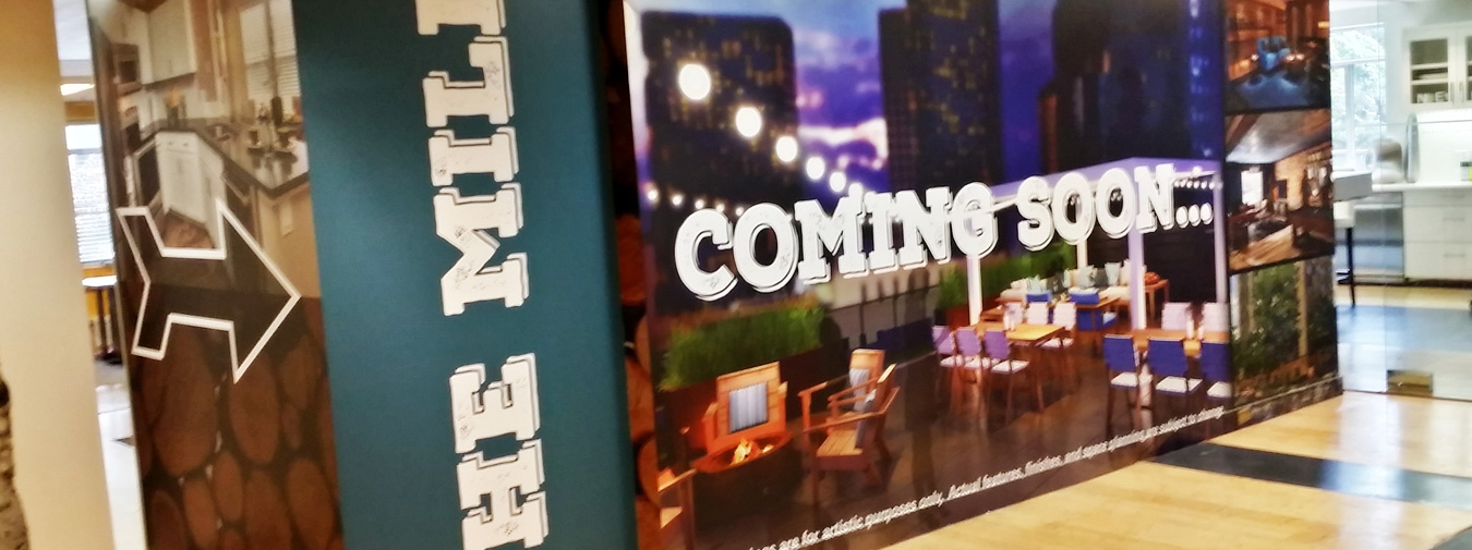 Indoor construction area with signage showing 'THE MILL' and 'COMING SOON...' featuring an outdoor patio design and arrow pointing left.