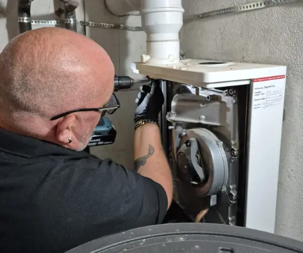 Technicien Techni-Therm intervenant sur une chaudière dans un local technique en Valais