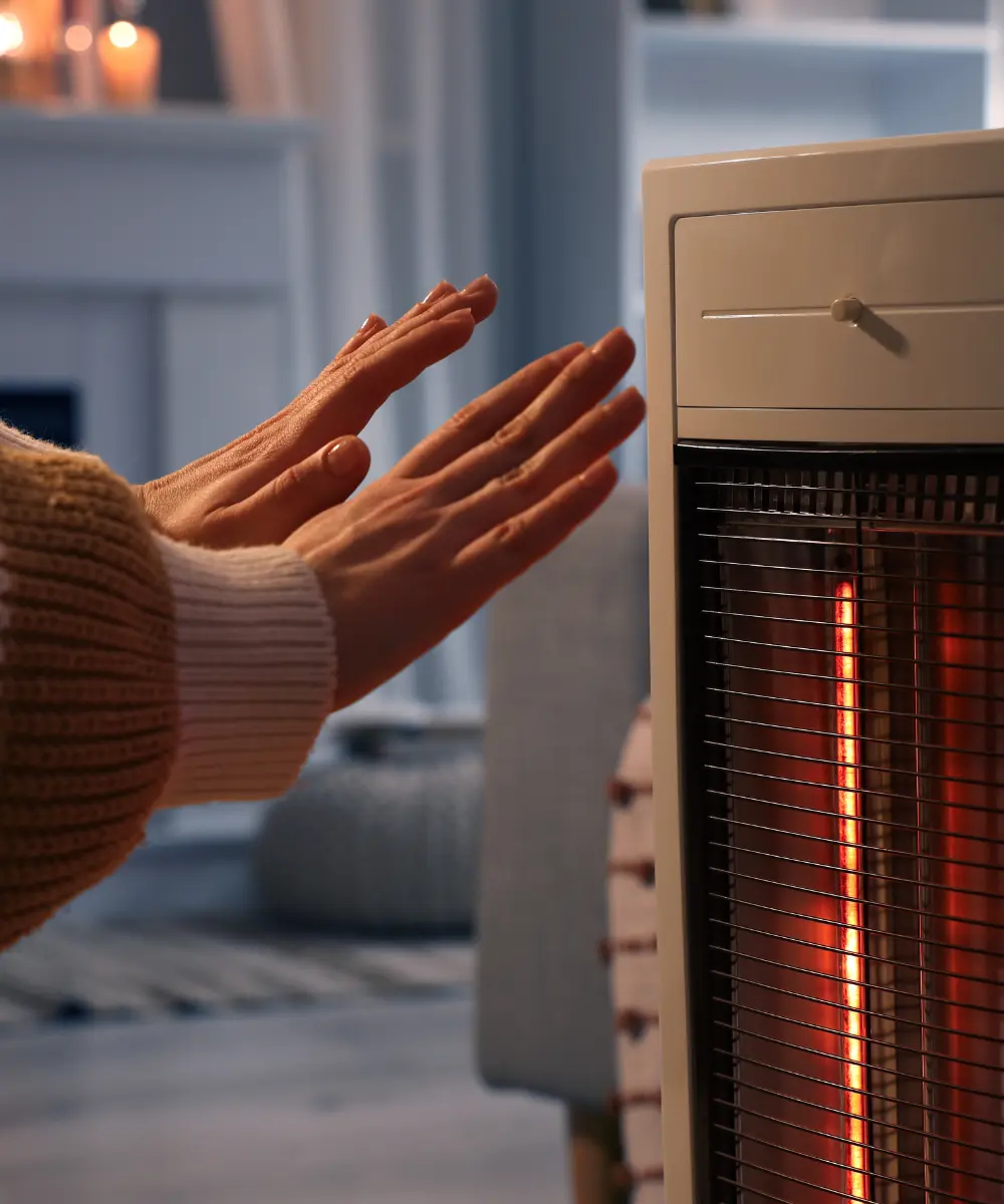 Personne se réchauffant les mains devant un radiateur électrique dans un salon