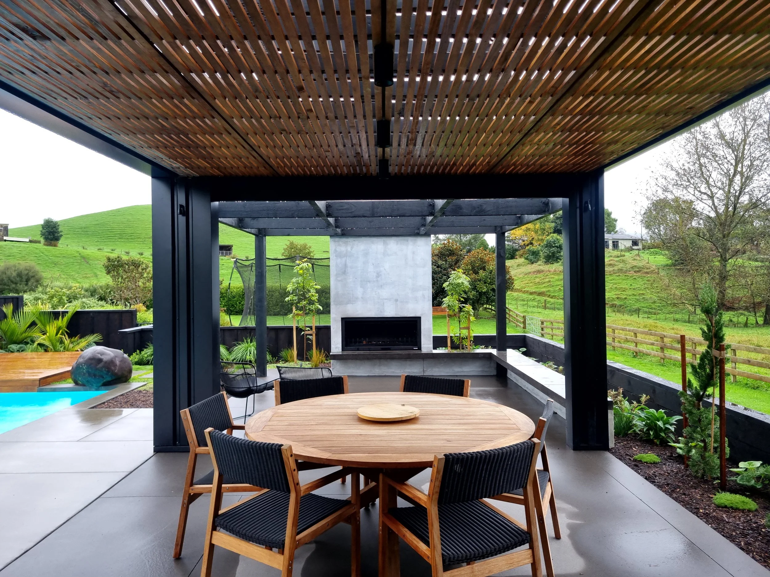 Timber-lined pergola with outdoor dining and fireplace, rural Waikato views