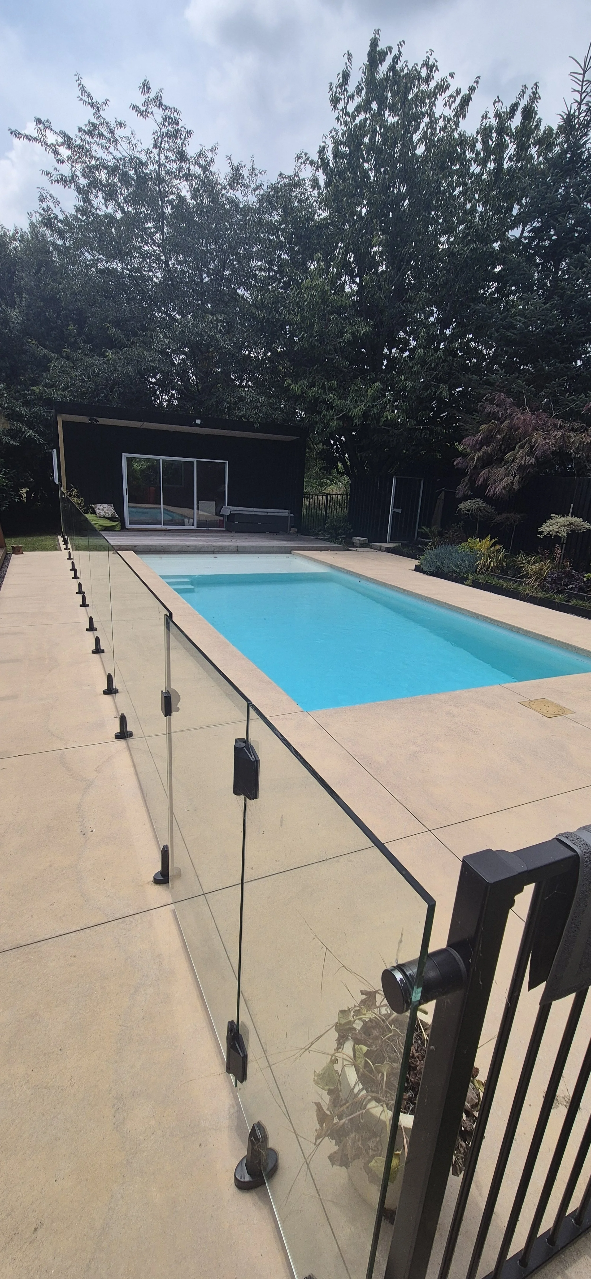 Concrete pool surround with frameless glass fencing, pool landscaping Waikato