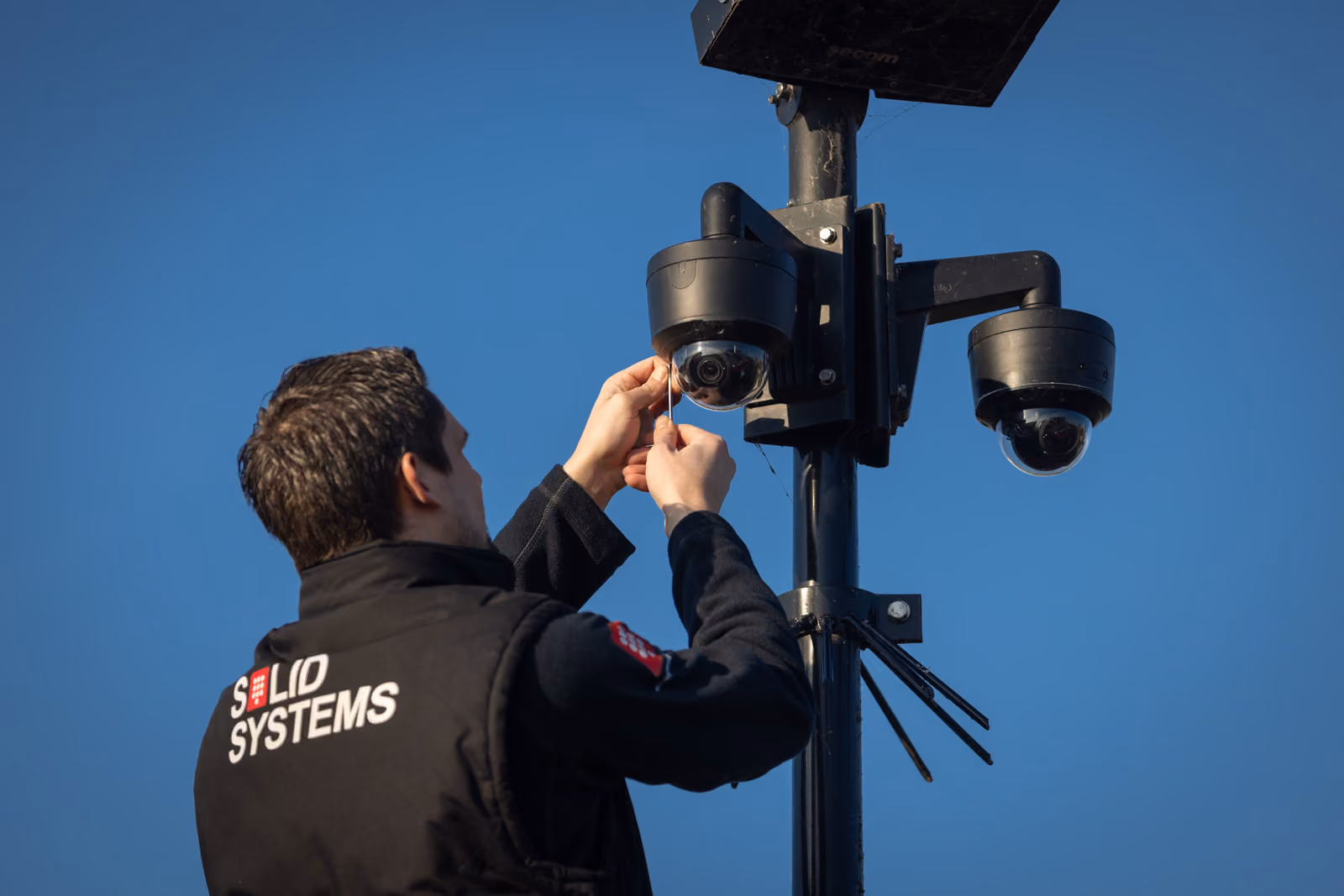 Een installatiemonteur van Solid Systems bevestigd camerabeveiliging in de buitenlucht.