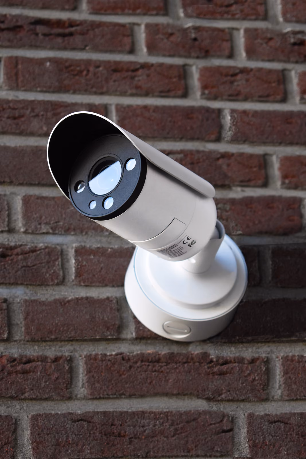 Een witte beveiligingscamera van Solid Systems buiten tegen een gemetselde muur. 
