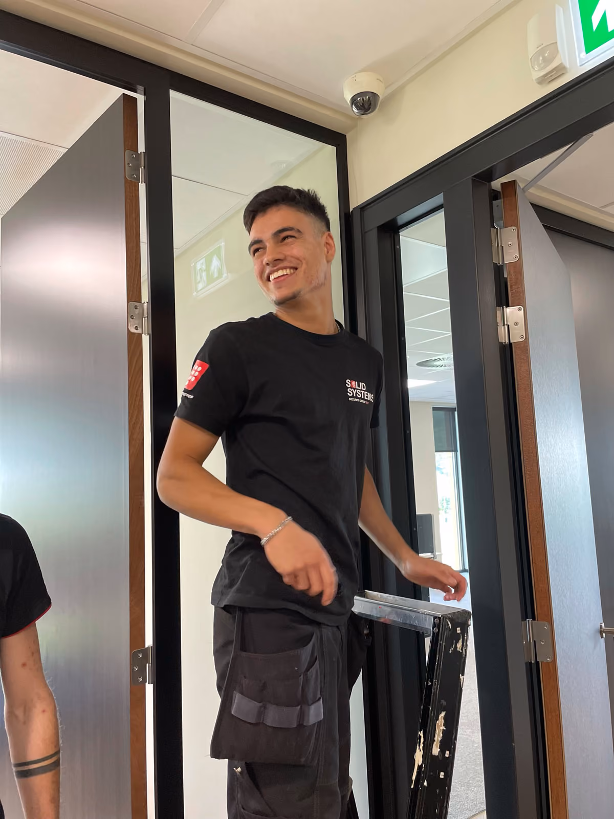 Trotse monteur van Solid Systems lachend op een ladder terwijl hij noodverlichting monteert aan het plafond.