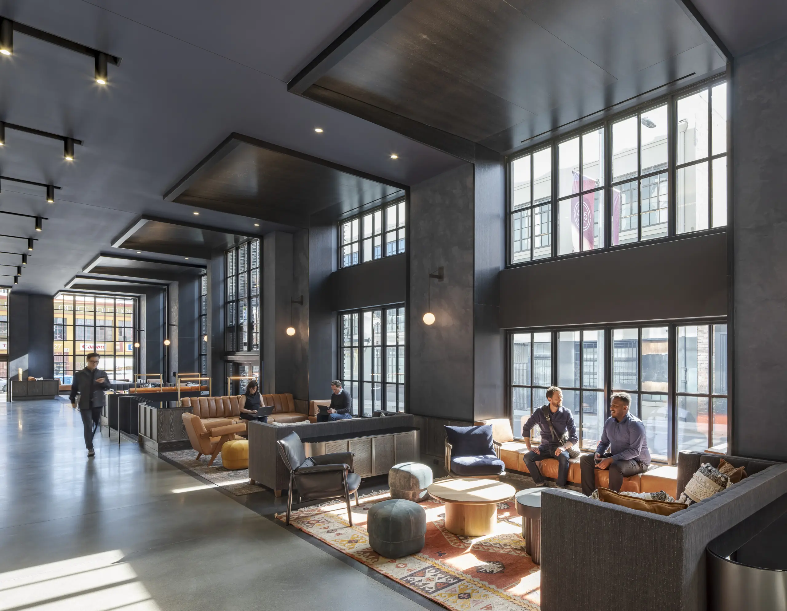 Een modern en industriële hotelomgeving met veel ramen, daglicht en pratende mensen.