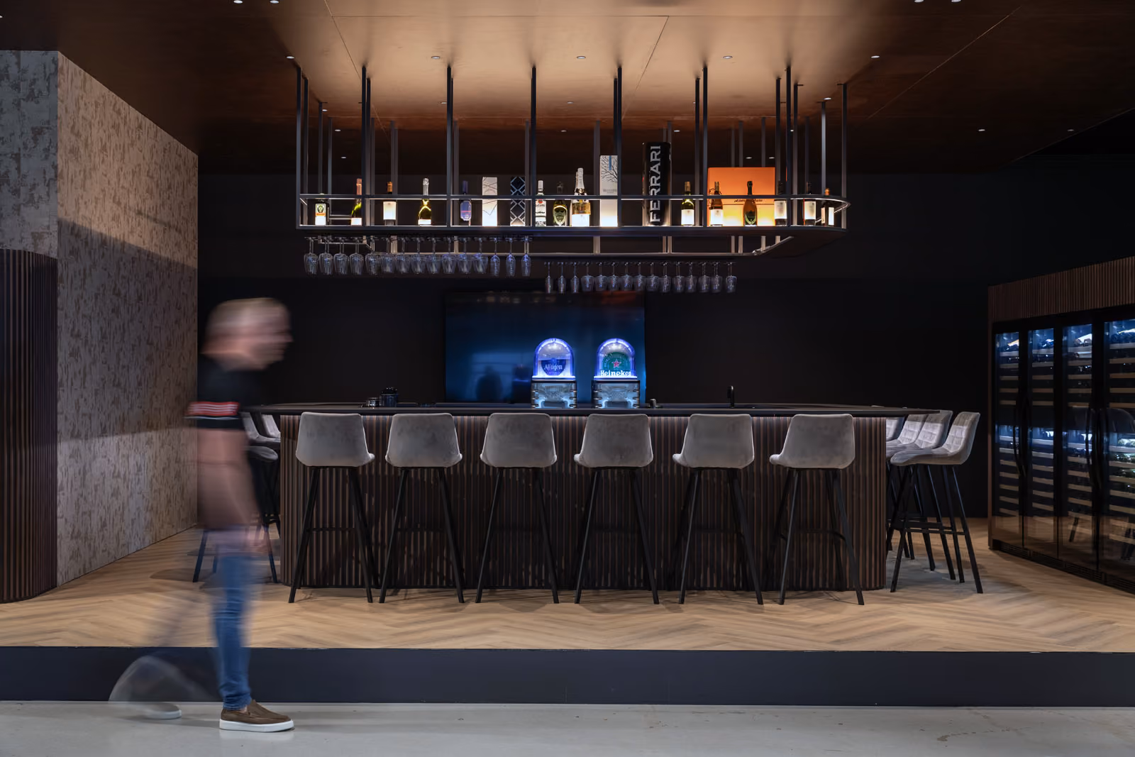 Een moderne, donkere maar aantrekkelijke bar met sfeerverlichting en meerdere barkrukken. 