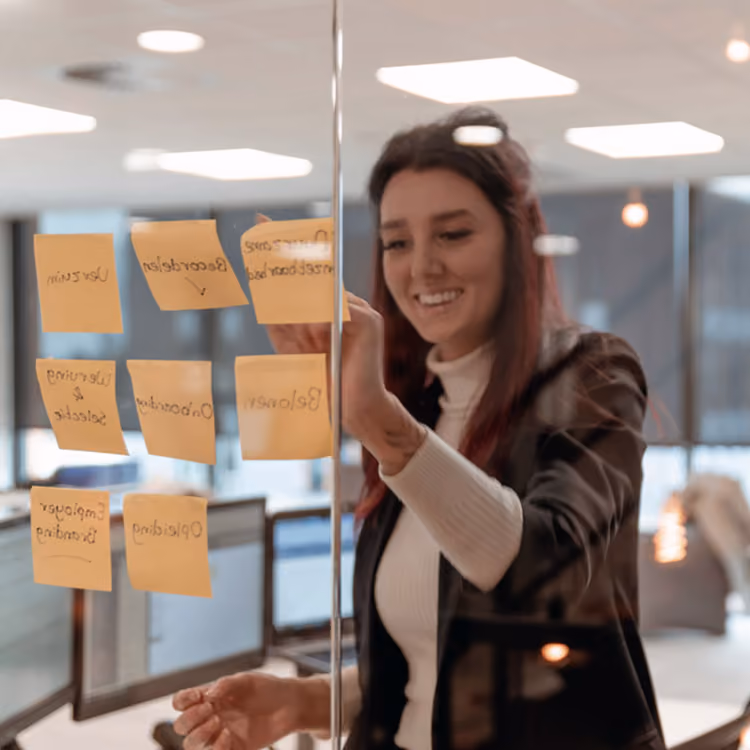 Lachende vrouw plakt gele memo's  op het raam tijdens een brainstormsessie bij Solid Systems.