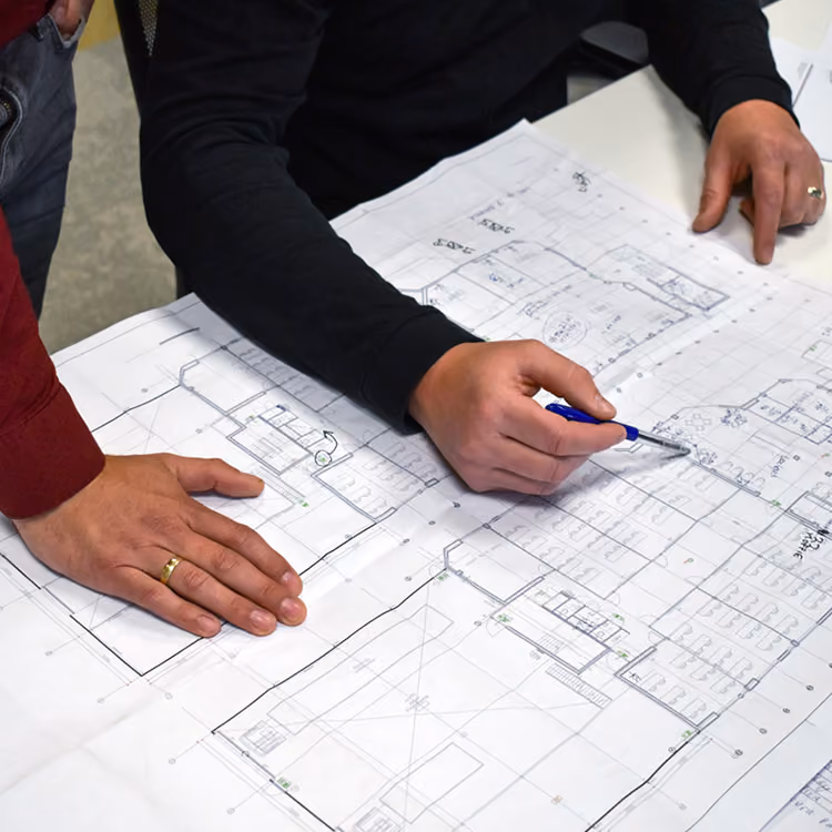 Werktekening op tafel terwijl meerdere collega's meekijken en een plan uitwerken.