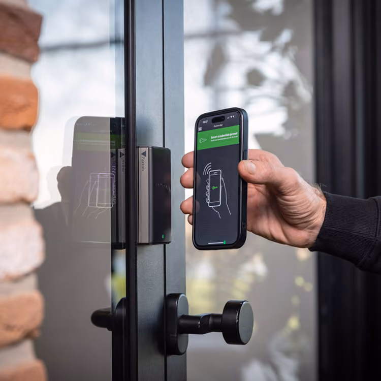 Hand met telefoon bij een deur met toegangscontrole en beveiliging van Solid Systems.
