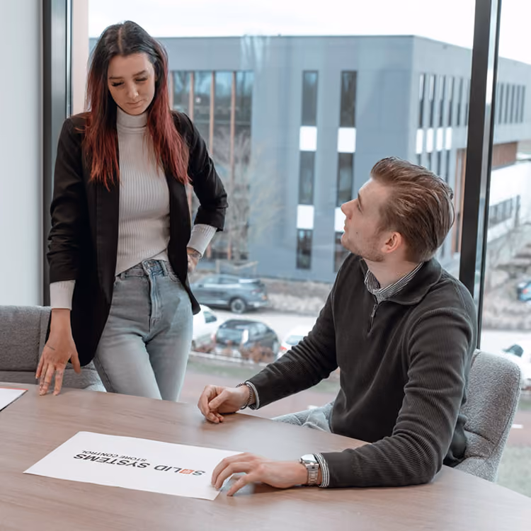 Overleg tussen een mannelijke en vrouwelijk medewerker van Solid Systems in een kantooromgeving.