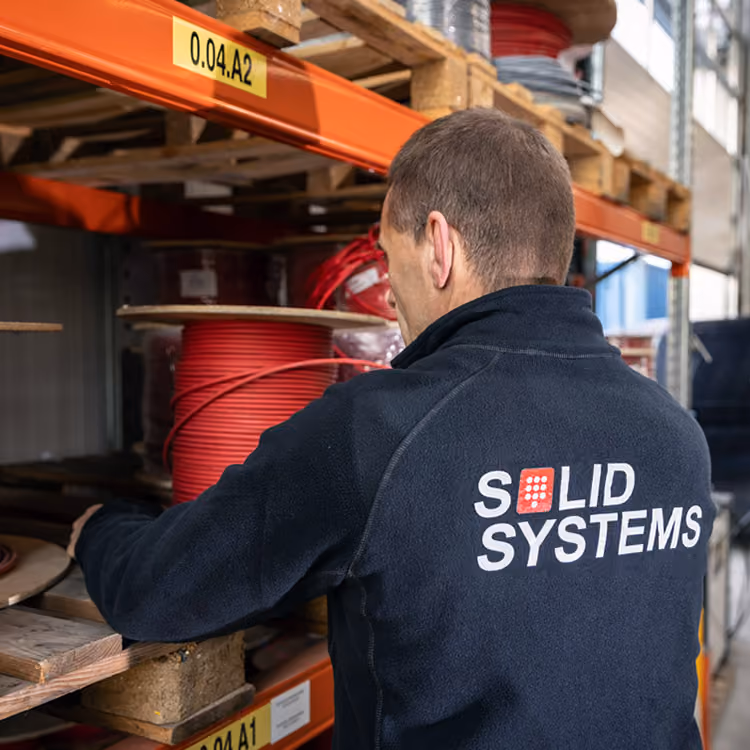 Een monteur van Solid Systems pakt benodigd materialen uit een schap in een opgeruimd magazijn.  