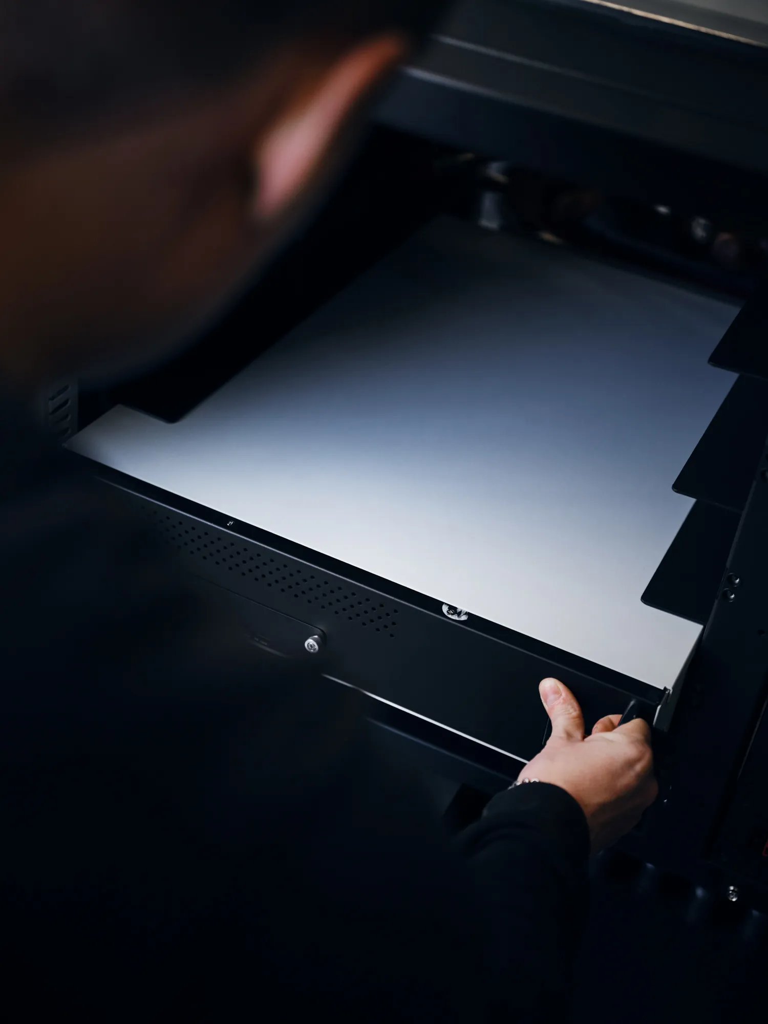 Person's hand pulling out a tray with white paper from a printer or copier machine.