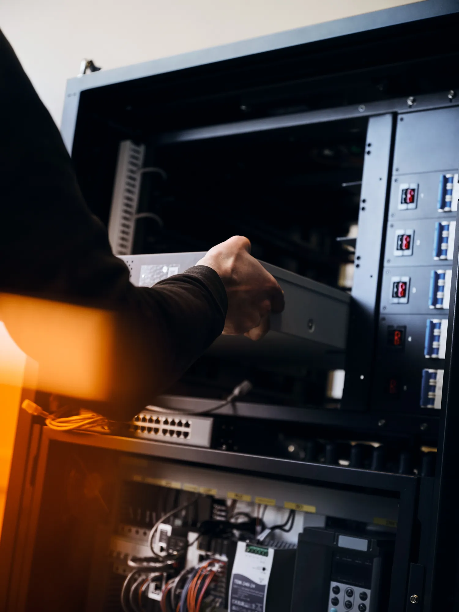 Person installing or removing a server or hardware component inside a server rack with various network cables and equipment.