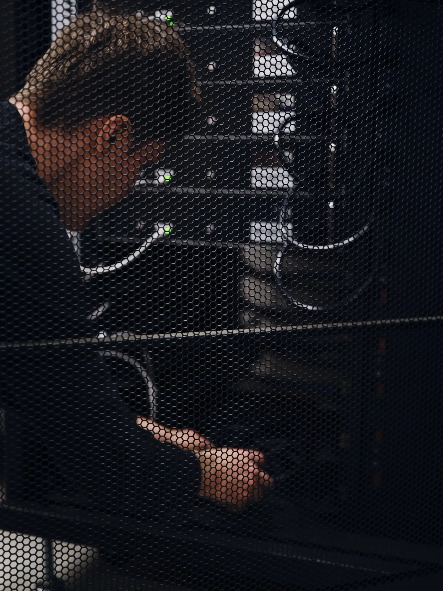 Technician working on server components behind a perforated metal panel with visible network cables and indicator lights.