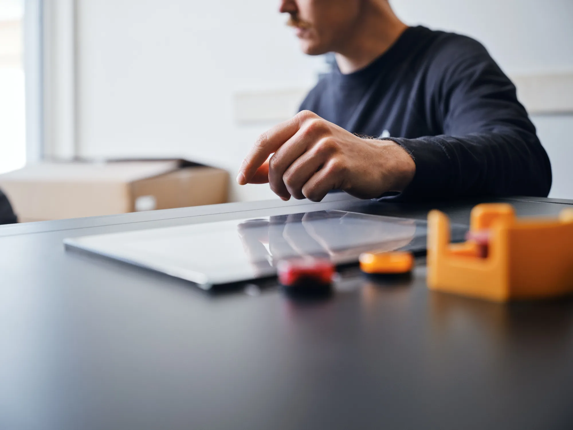 Man using a digital tablet with his finger on a black table with blurred office items.