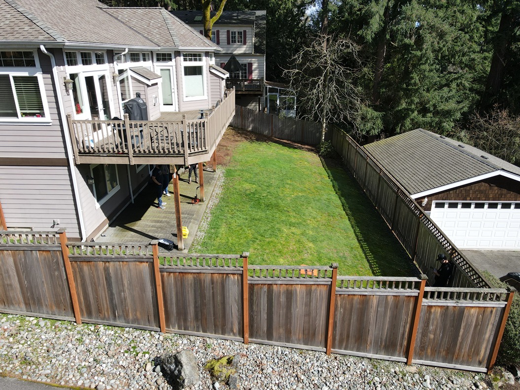 A bare backyard surrounded with a simple lawn and contractors surveying the area