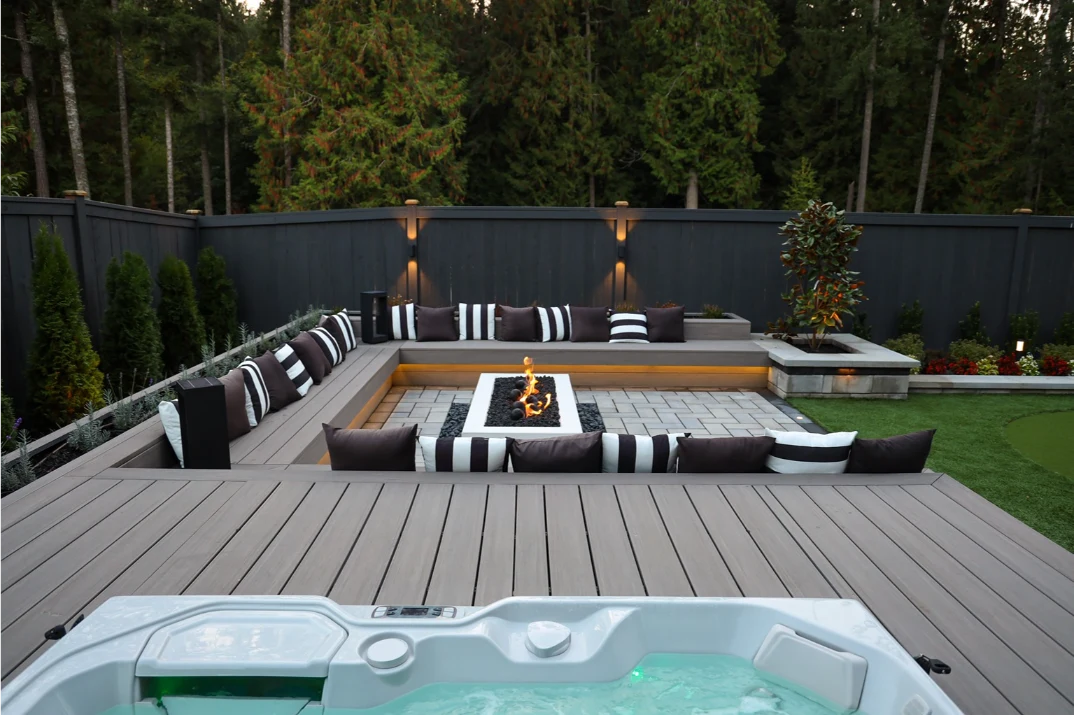Sunken paver lounge with a white linear fire table, built-in bench seating, LED accent lighting, and an adjacent hot tub deck