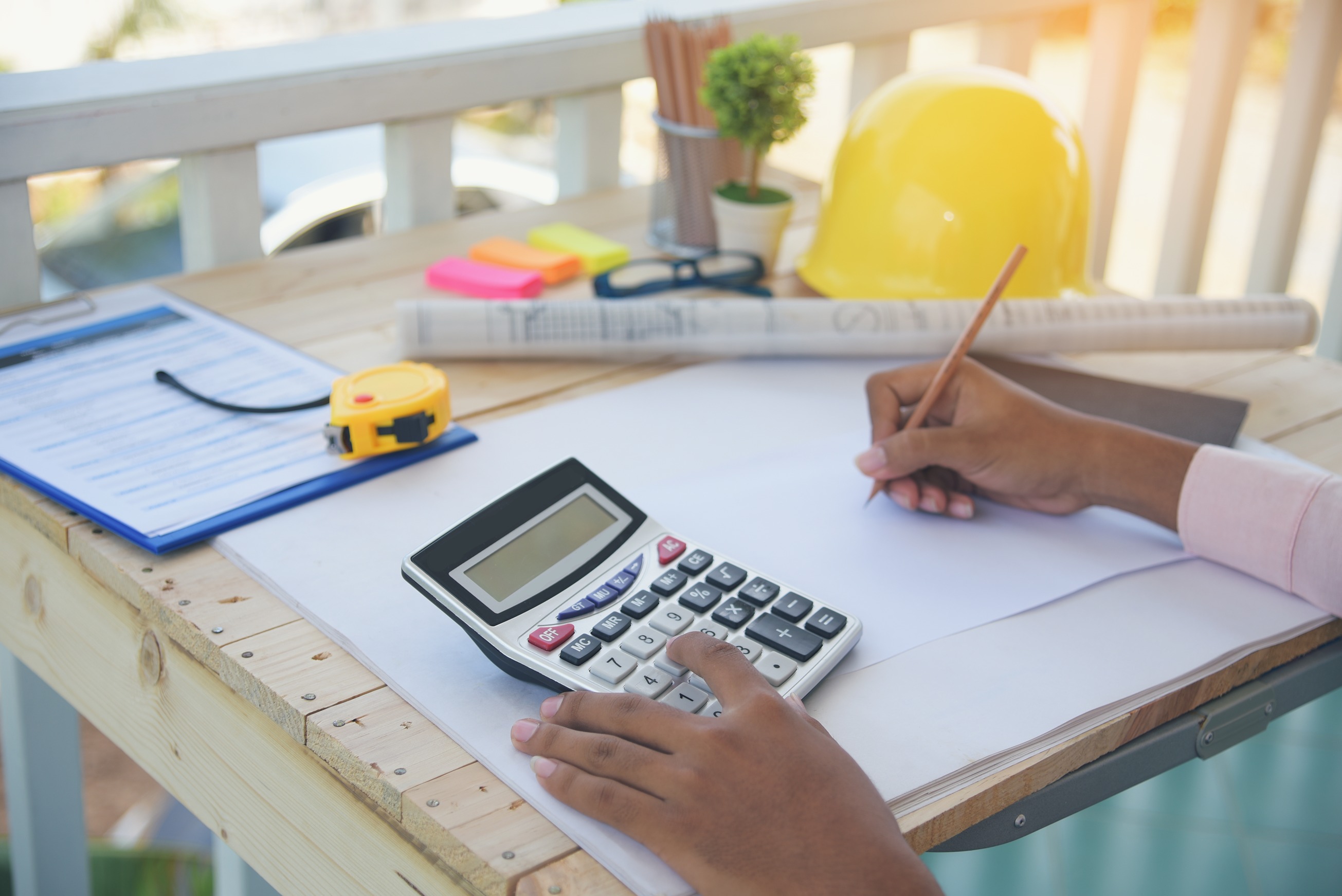 Blueprints, yellow hard hat, and calculator on a desk.