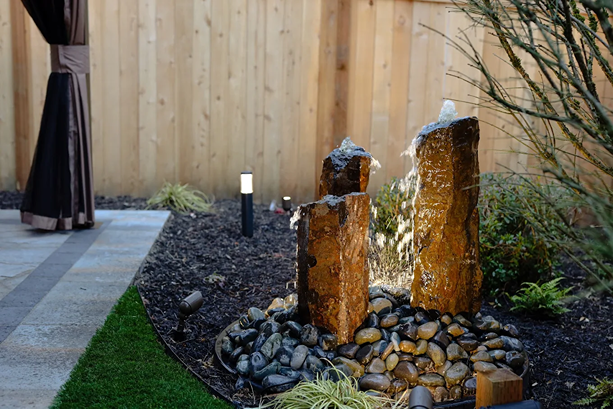 Rock water feature with river stones in garden bed.