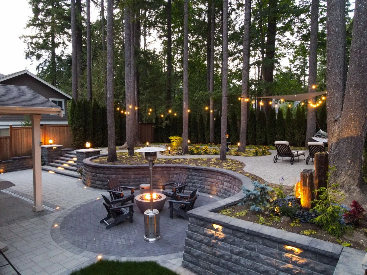 Custom paver patio with fire pit lounge, string lights, and retaining wall
