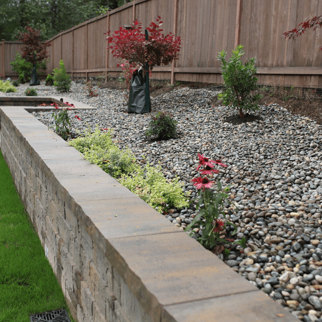 Angkorscape professional backyard landscaping design with granite retaining walls, layered garden beds, ornamental trees, and a modern patio fire pit