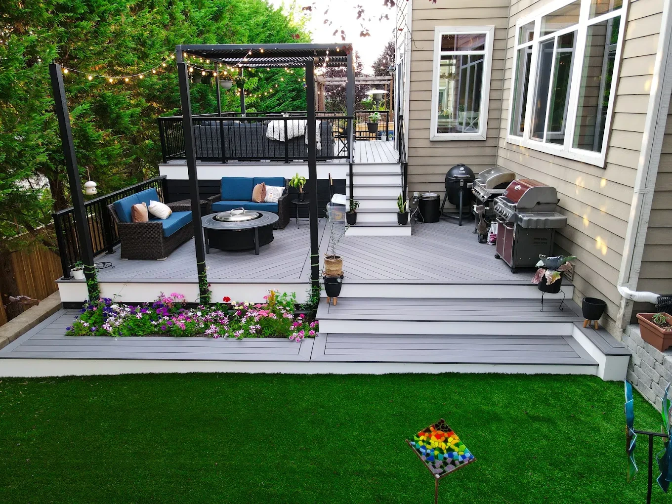 A multi-level deck with a pergola, string lights, and a colorful flower garden in Snoqualmie.