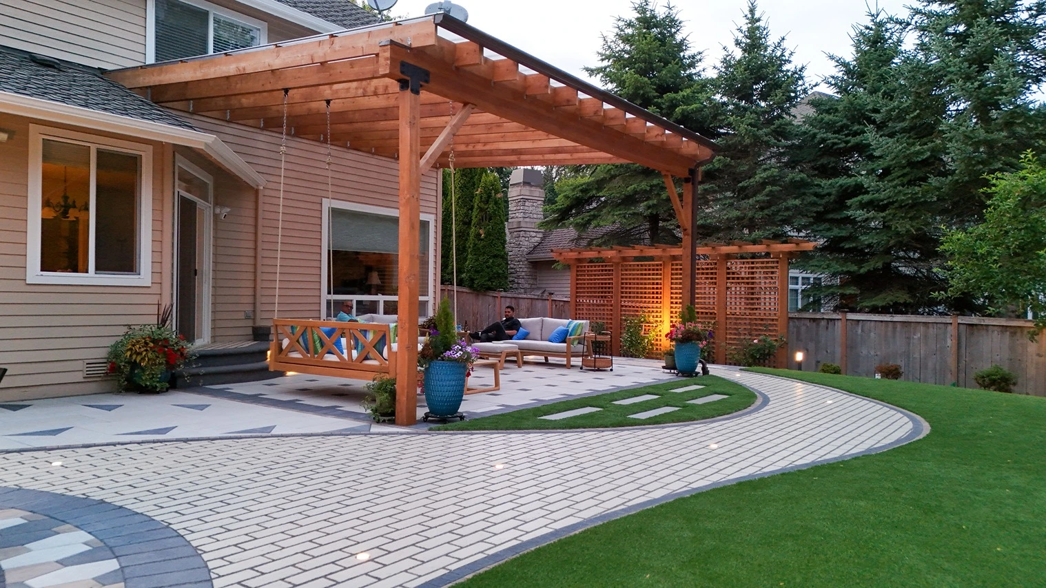 A Newcastle backyard after renovation, with a paver patio, bench seating, and string lights in the evening.