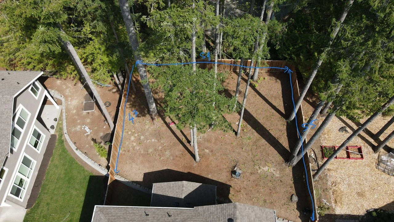 Aerial view of a Snoqualmie yard before renovation, with bare ground, tall trees, and a wooden deck structure.
