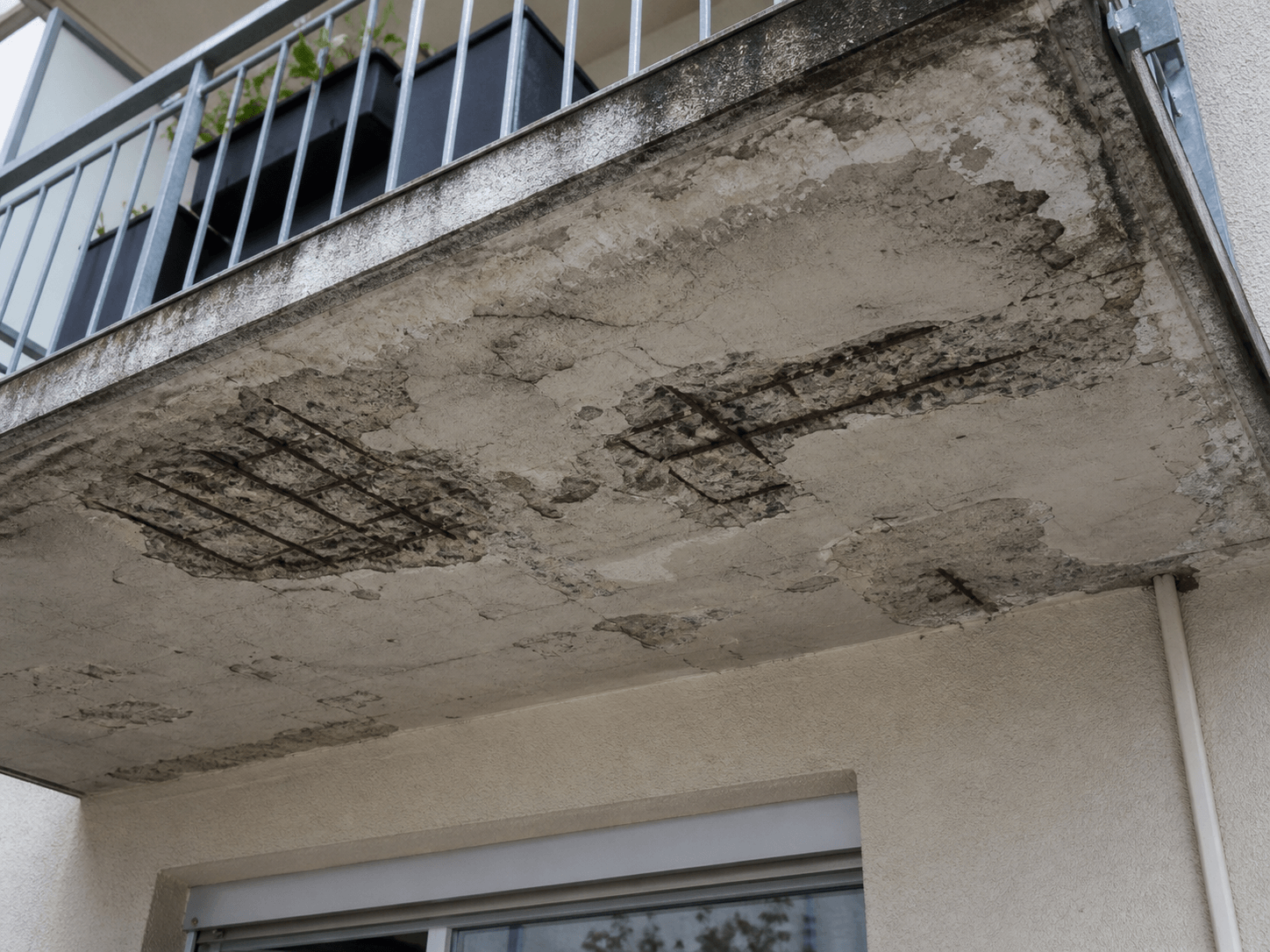 Betonbalkon mit sichtbaren Schäden und freiliegenden Rostbewehrungen unter der Platte.