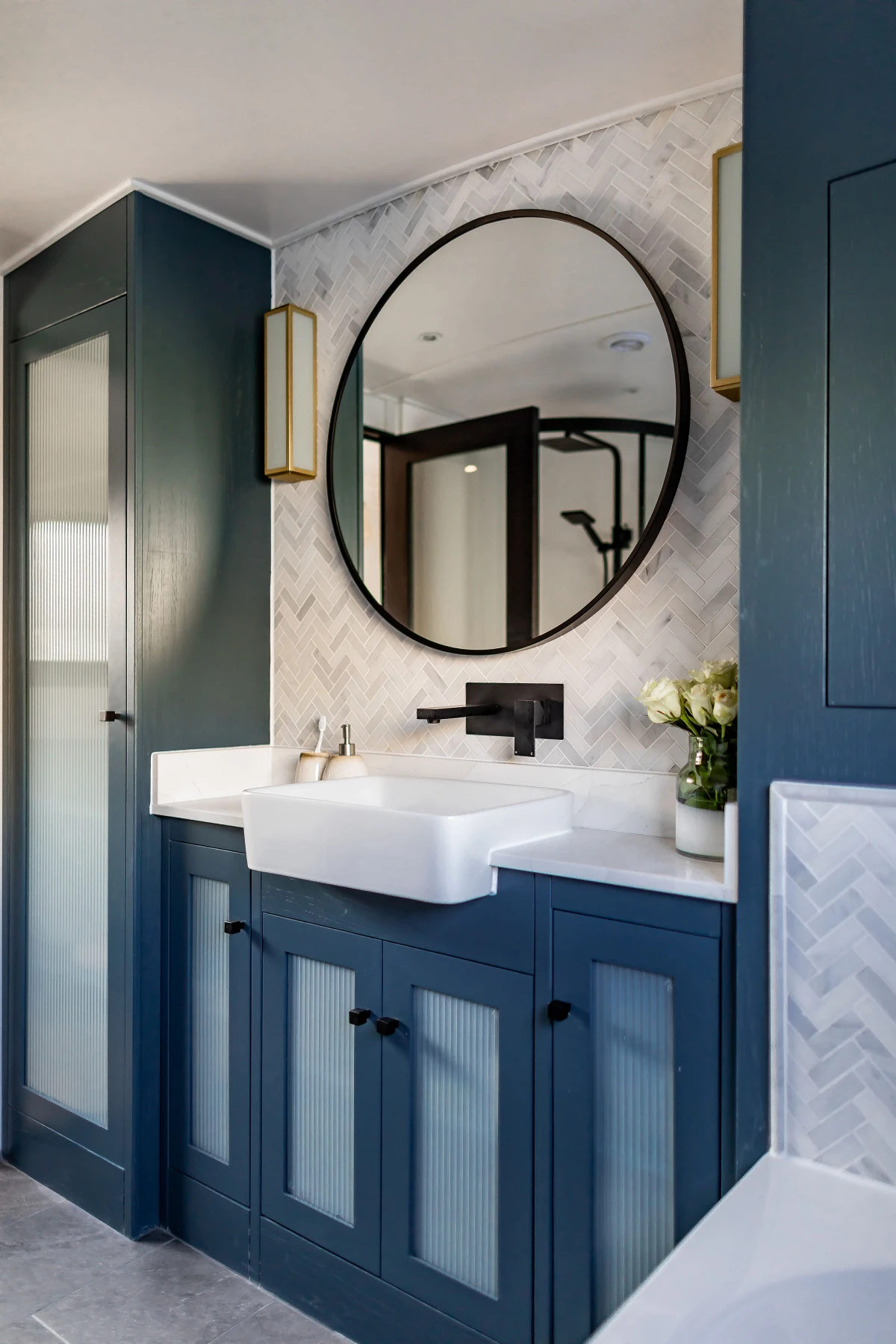 Modern bathroom vanity with navy blue cabinets, a white rectangular sink, round mirror, and wall-mounted black faucet.