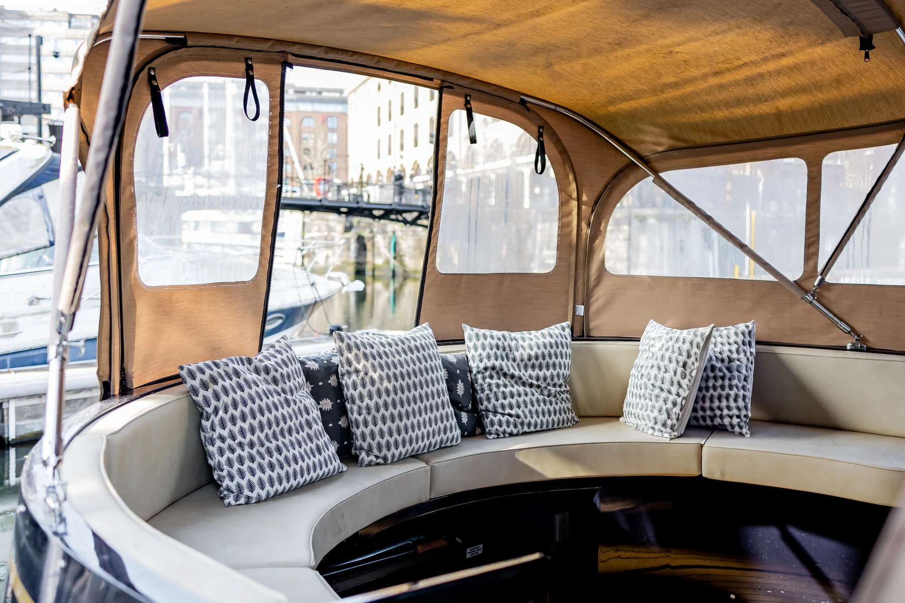 Curved beige boat seating area with patterned cushions under a tan canopy at a marina.