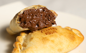 Baked empanada filled with melted chocolate custard on a white plate.