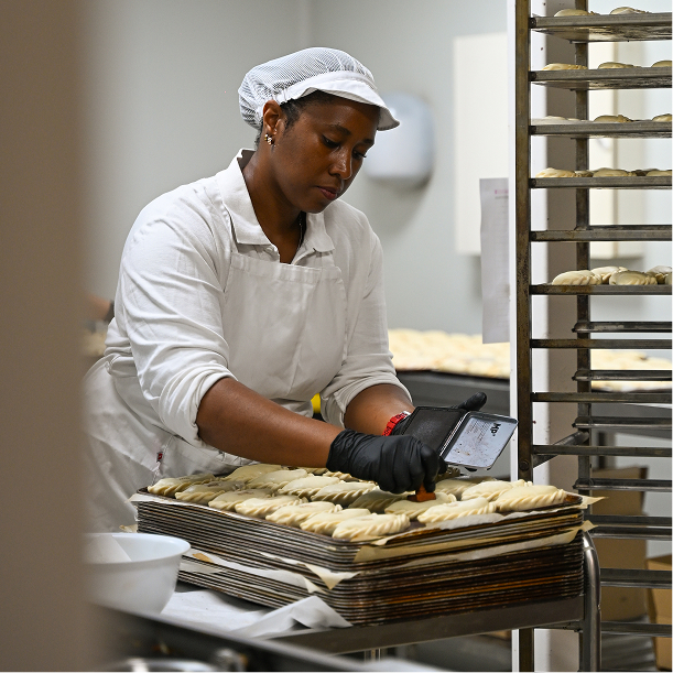Female baker in white uniform preparing dough on trays in an industrial kitchen.