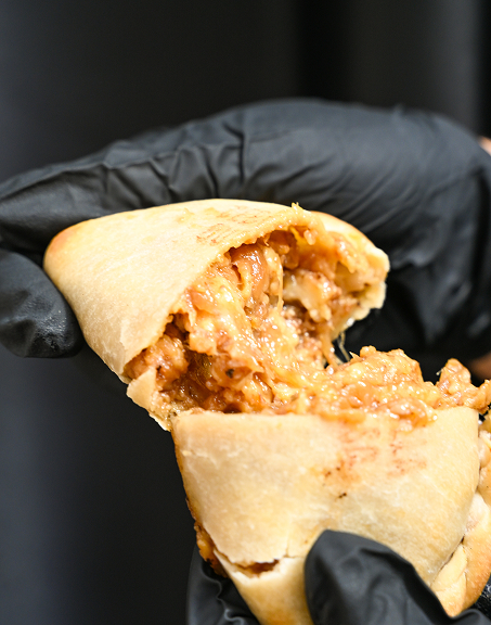 Hand in black glove holding a stuffed pita bread filled with melted cheesy minced meat.