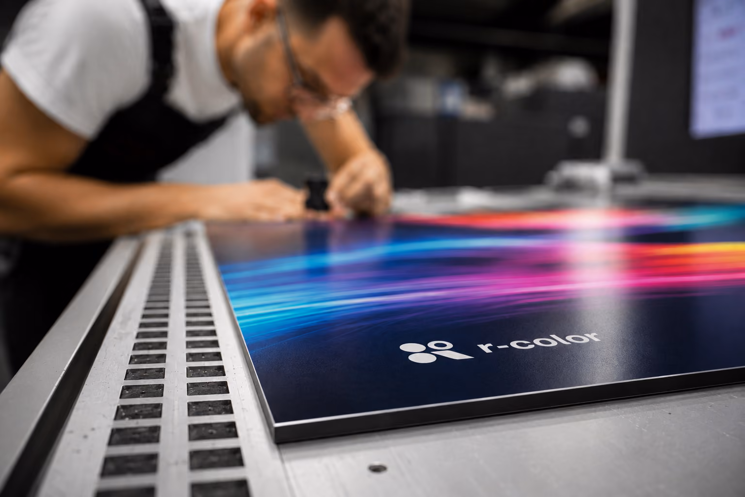 Mann begutachtet einen großen Druck mit bunten Linien auf einem Tisch mit r-color Logo.