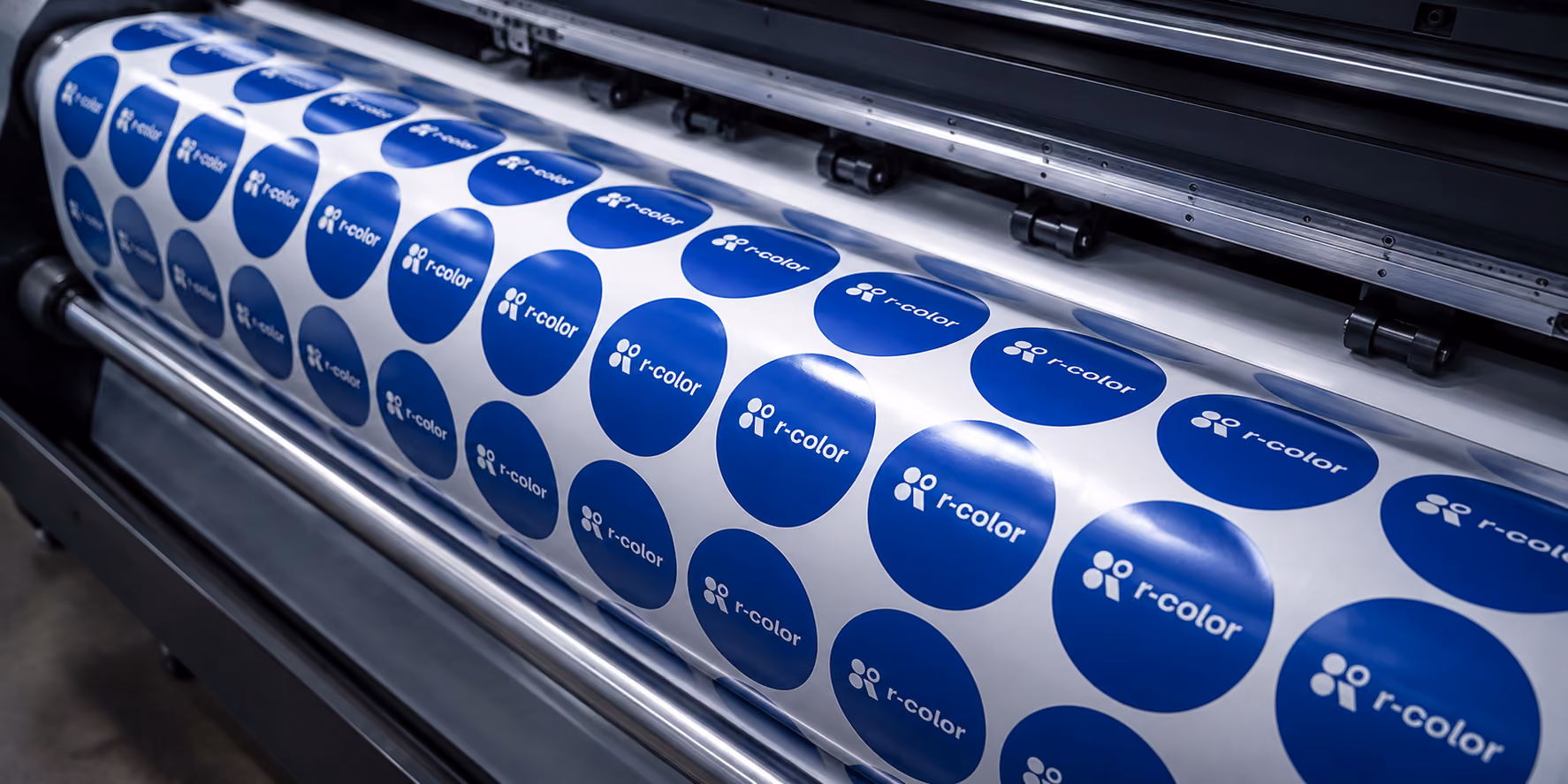 Digitaldruckmaschine, die blaue r-color-Logos als Aufkleber auf einer Rolle druckt.
