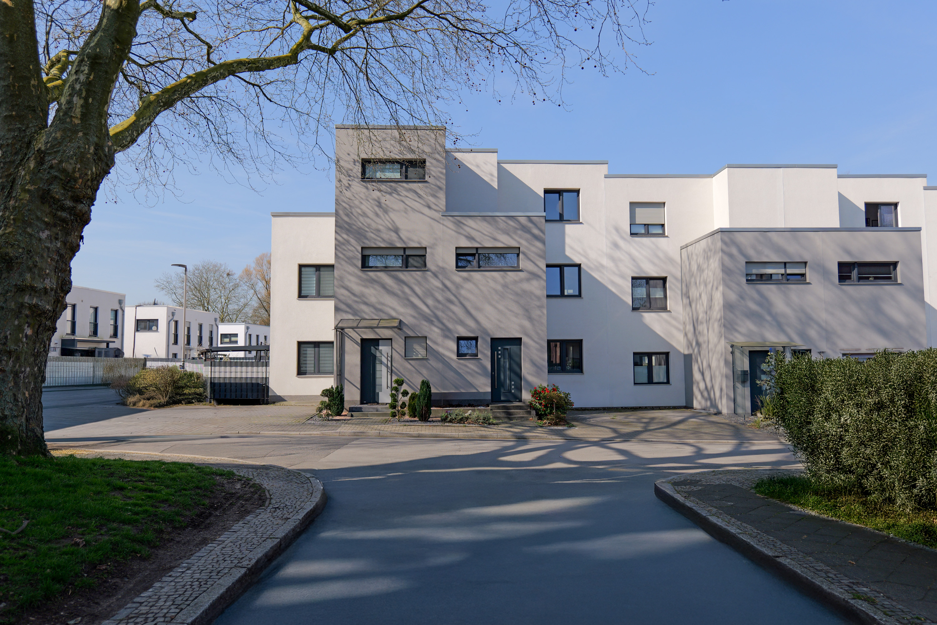 Moderne weiße Mehrfamilienhäuser mit klaren Linien an einer ruhigen Straße bei sonnigem Himmel.