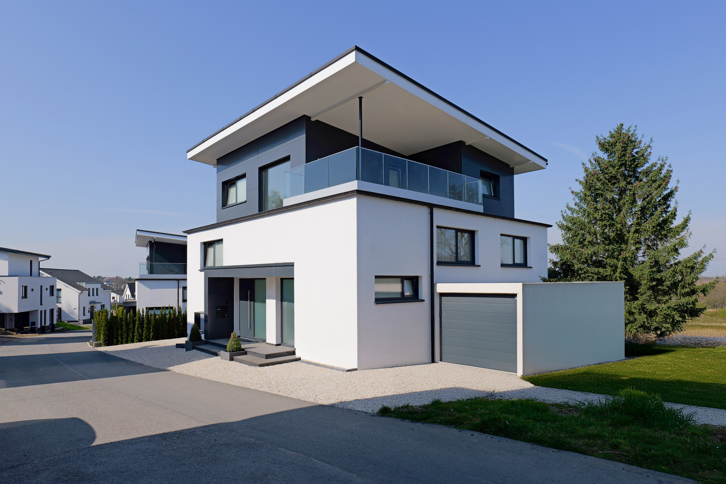 Modernes weißes Haus mit schwarzer Verkleidung, Garage und großem Balkon bei klarem Himmel.