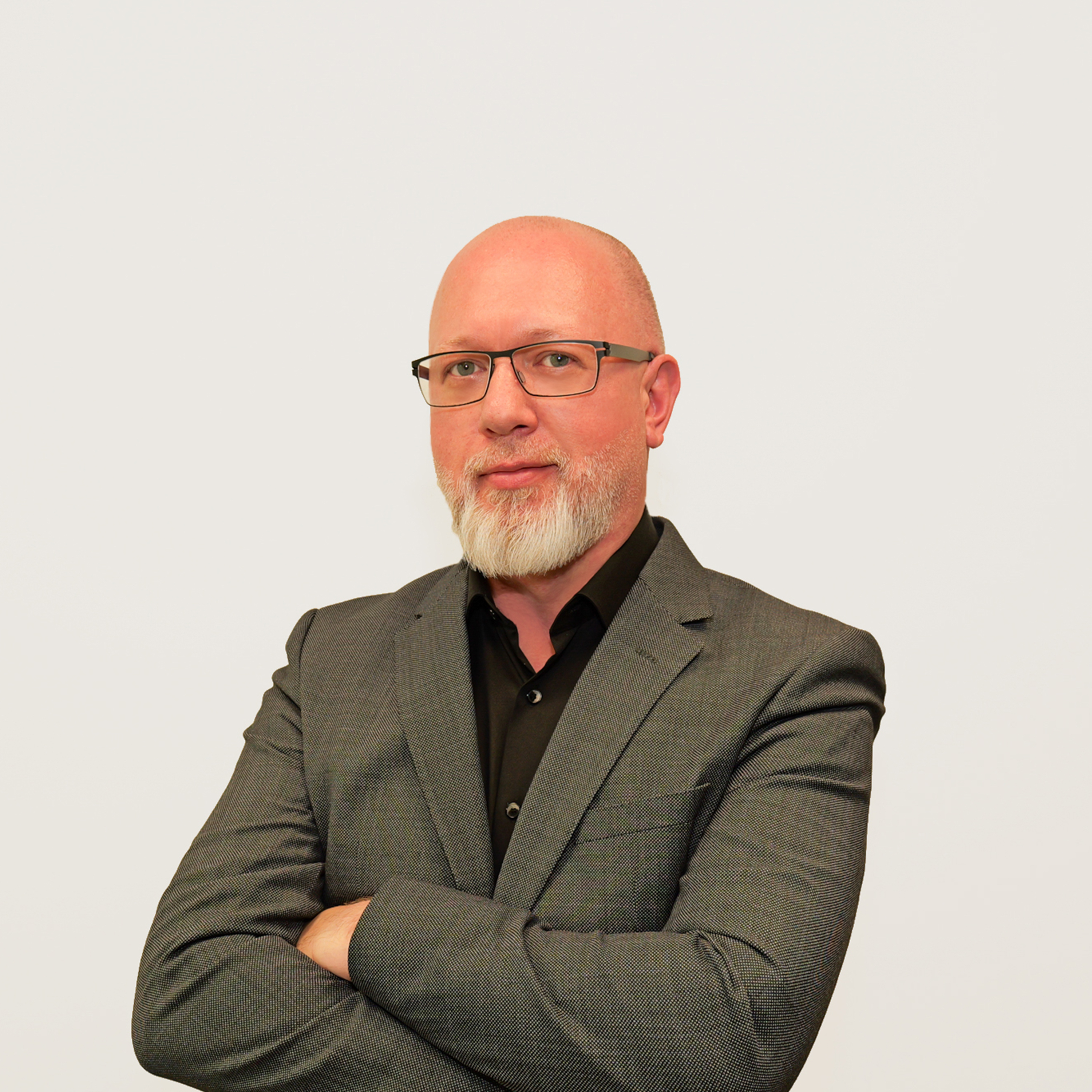 Mann mit Brille, grauem Anzug und weißem Bart vor weißem Hintergrund.