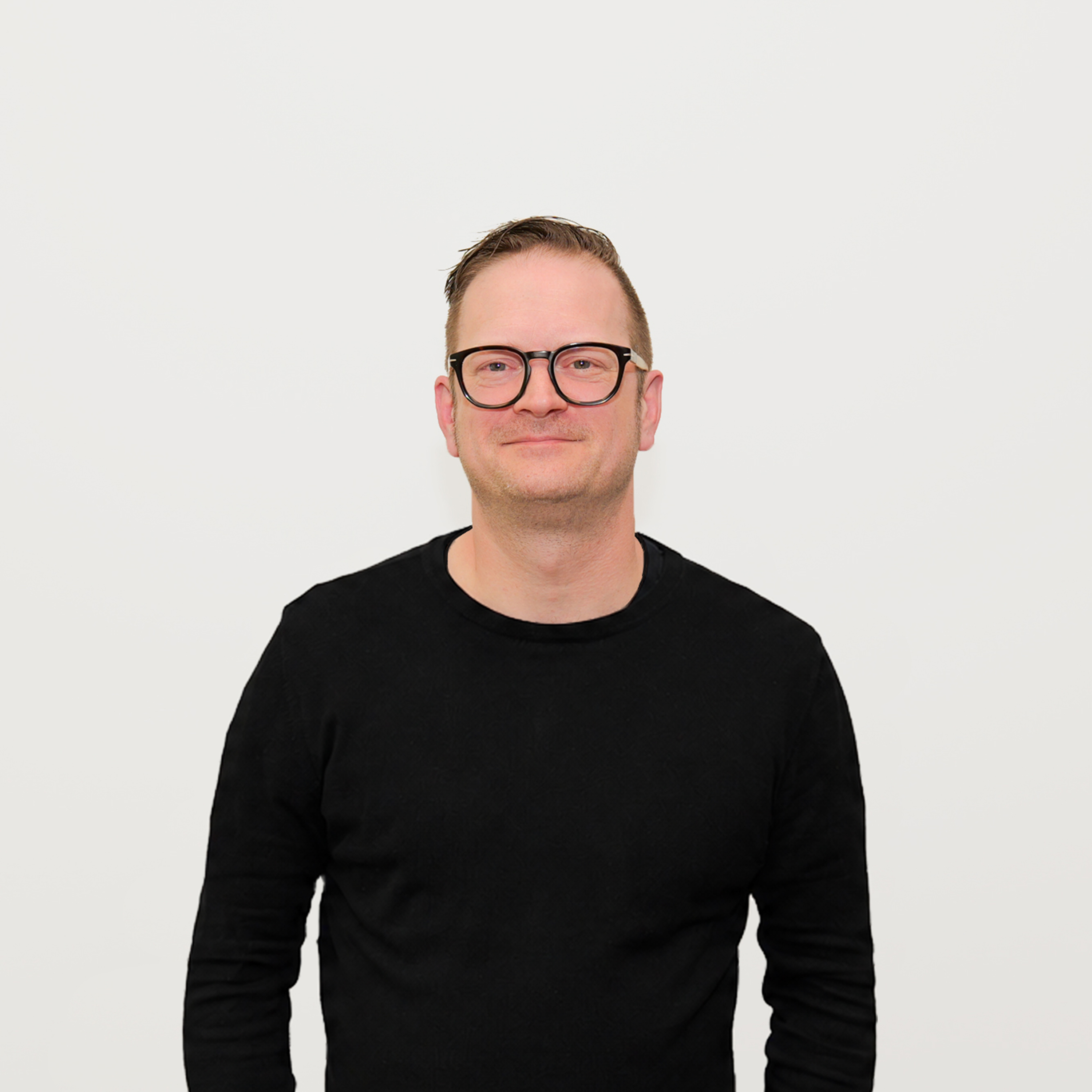 Mann mit schwarzem Pullover und Brille vor weißem Hintergrund.
