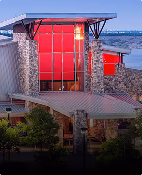Modern stone building with large red window panels and metal roof at dusk.