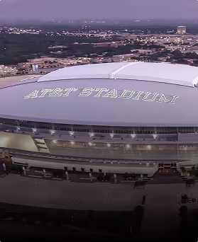 Aerial view of AT&T Stadium's roof with cityscape in the distant background at dusk.