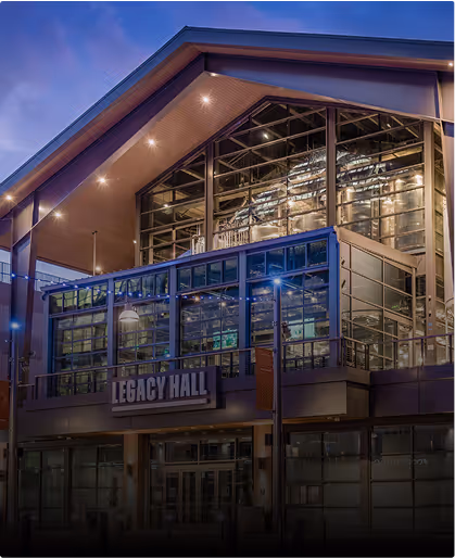 Modern building named Legacy Hall with large glass windows reflecting lights at dusk.