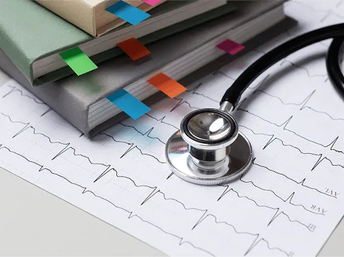 Stethoscope resting on an electrocardiogram printout with notebooks marked by colorful tabs in the background.