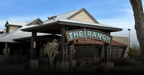 Entrance sign for The Ranch Las Colinas with building and clear sky in the background.