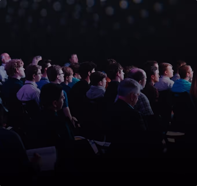 Audience seated in rows attentively watching an event or presentation in a darkened room.